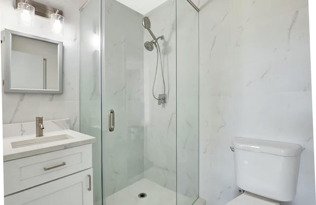 full bath with toilet, a marble finish shower, tile walls, and vanity