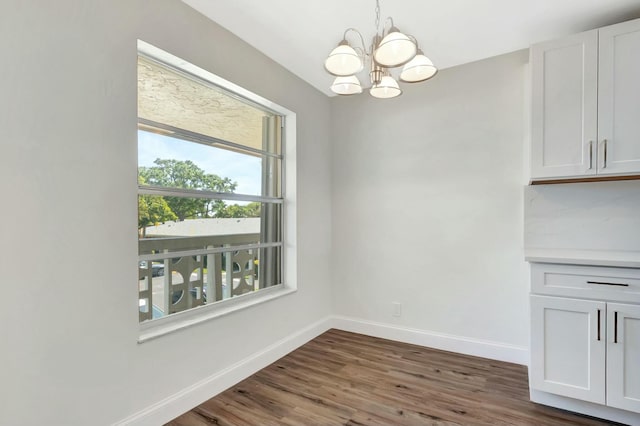 unfurnished dining area with a notable chandelier, dark wood-style flooring, and baseboards