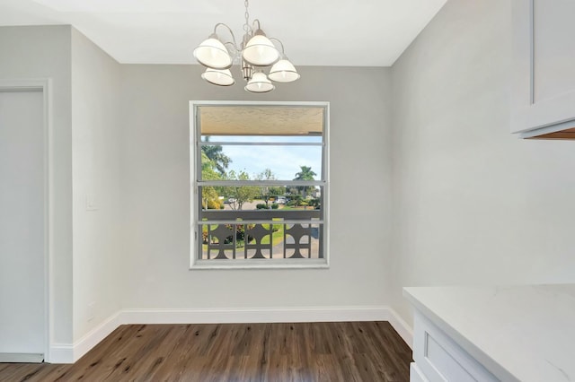 unfurnished dining area with a notable chandelier, dark wood-style floors, and baseboards