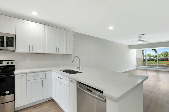 kitchen featuring stainless steel appliances, a peninsula, a sink, light wood-style floors, and open floor plan