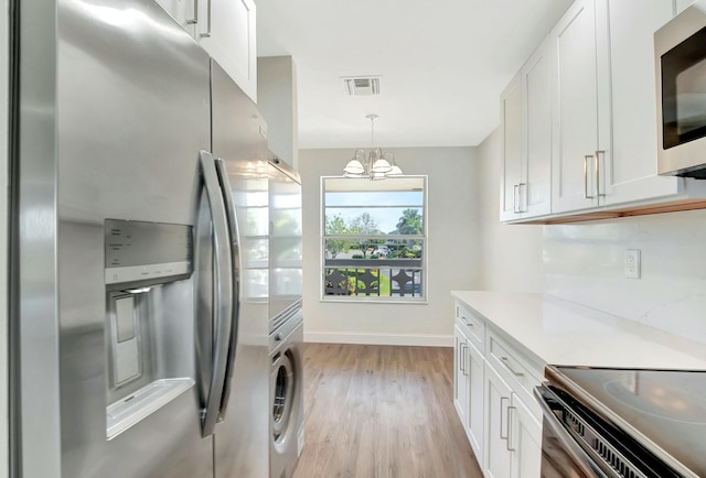 kitchen with stainless steel appliances, visible vents, white cabinetry, stacked washing maching and dryer, and light wood-type flooring