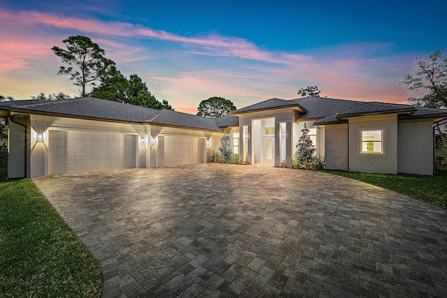 prairie-style house with a garage, decorative driveway, and stucco siding