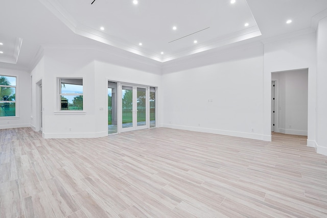 unfurnished living room featuring light wood-style flooring, a raised ceiling, crown molding, and a towering ceiling