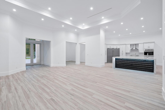 unfurnished living room with light wood finished floors, ornamental molding, a high ceiling, french doors, and recessed lighting