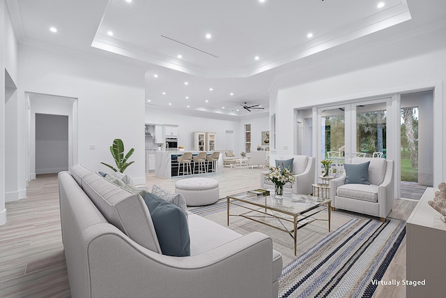 living area featuring light wood-style flooring, a tray ceiling, ornamental molding, and a towering ceiling