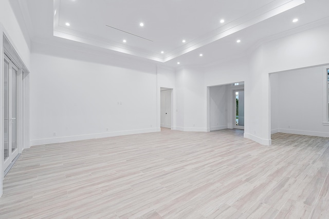 spare room with a towering ceiling, a tray ceiling, crown molding, light wood-type flooring, and recessed lighting