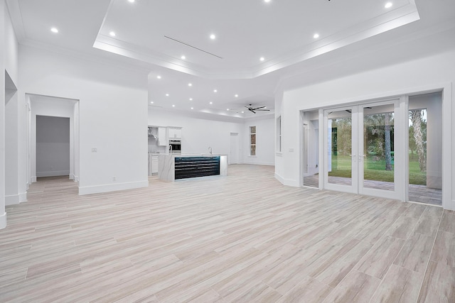 unfurnished living room featuring a tray ceiling, a towering ceiling, ornamental molding, ceiling fan, and light wood-type flooring