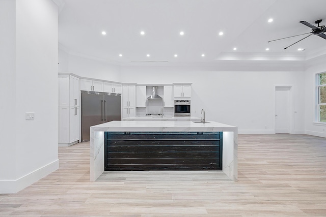 kitchen with a sink, wall chimney range hood, a large island, stainless steel built in refrigerator, and crown molding