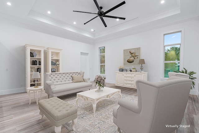 living room featuring light wood-style floors, a raised ceiling, ornamental molding, and a ceiling fan