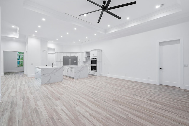 unfurnished living room featuring ceiling fan, light wood-style flooring, a raised ceiling, and crown molding