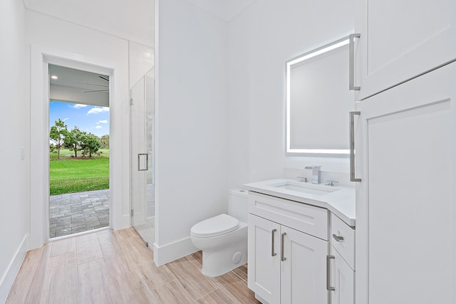 bathroom with toilet, vanity, a shower stall, wood finished floors, and baseboards