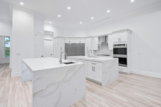 kitchen with appliances with stainless steel finishes, ornamental molding, a sink, wall chimney range hood, and a large island with sink