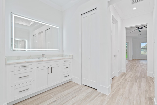 bathroom with baseboards, ceiling fan, wood finished floors, crown molding, and vanity