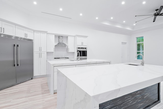 kitchen featuring a spacious island, wall chimney exhaust hood, stainless steel appliances, white cabinetry, and a sink