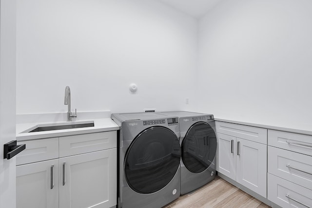 clothes washing area with cabinet space, washing machine and dryer, light wood-style floors, and a sink