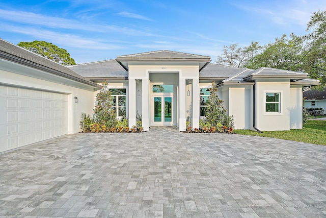 prairie-style house with french doors, decorative driveway, an attached garage, and stucco siding