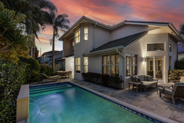 back of property at dusk with stucco siding, a patio, a fenced in pool, and outdoor lounge area