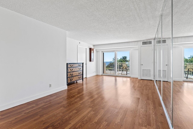 unfurnished living room with visible vents, baseboards, a textured ceiling, and wood finished floors
