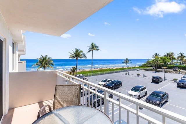 balcony featuring a beach view, outdoor dining area, and a water view