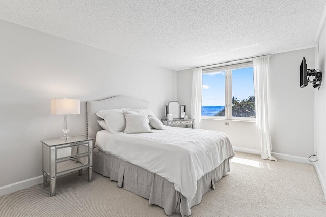 bedroom featuring baseboards, light colored carpet, and a textured ceiling