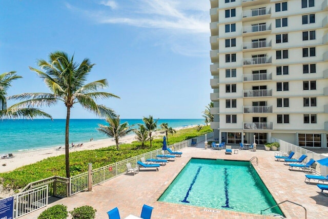 community pool with a beach view, a patio area, fence, and a water view