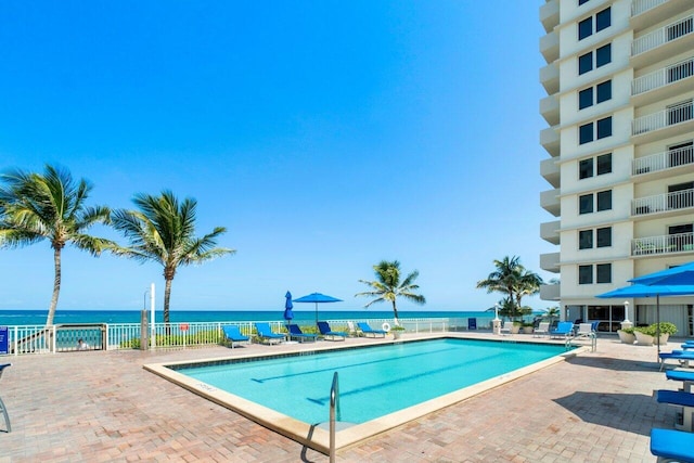 community pool with a patio area, a water view, and fence