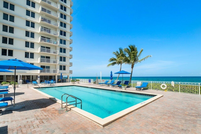 pool with a patio, a water view, and fence