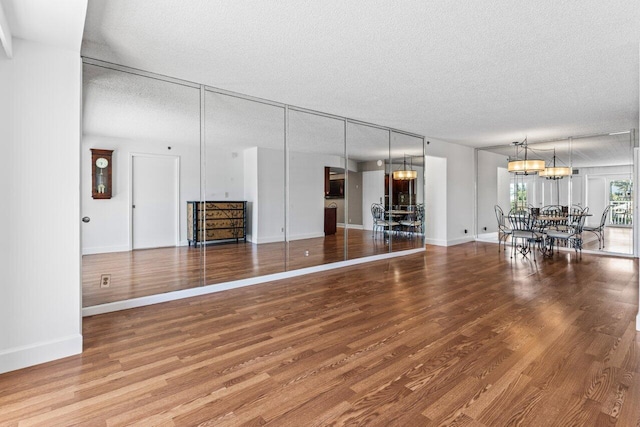 unfurnished living room featuring baseboards, wood finished floors, a textured ceiling, and a chandelier