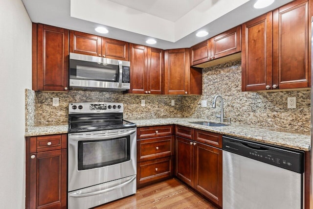 kitchen with light wood-style flooring, a sink, light stone counters, tasteful backsplash, and appliances with stainless steel finishes