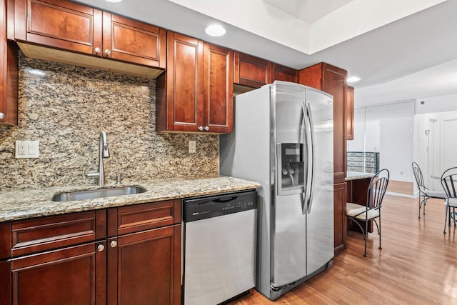 kitchen with light stone countertops, light wood-type flooring, decorative backsplash, stainless steel appliances, and a sink