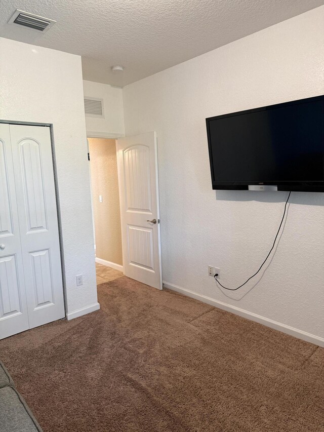 unfurnished bedroom with a textured ceiling, carpet floors, visible vents, baseboards, and a closet