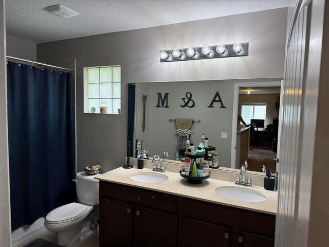 bathroom with toilet, double vanity, a textured ceiling, and a sink