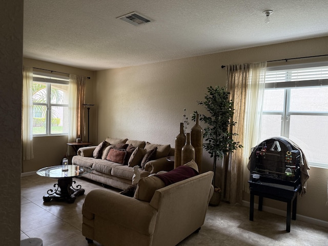 living area featuring visible vents, a textured wall, a textured ceiling, baseboards, and tile patterned floors