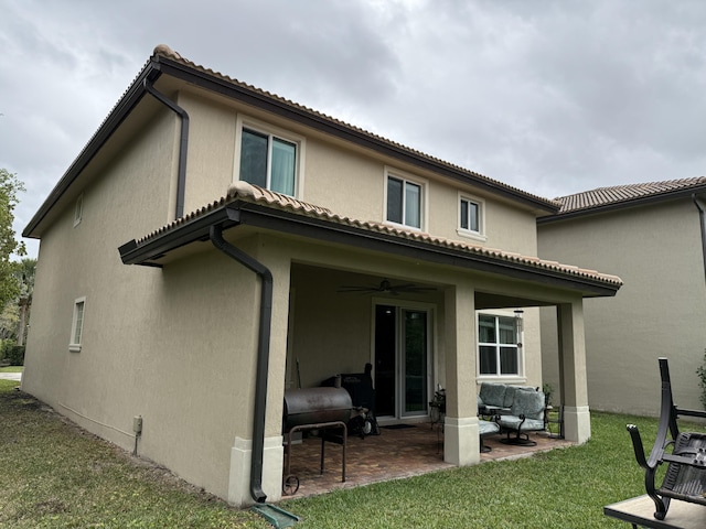 rear view of house with a tile roof, stucco siding, a patio, and a lawn