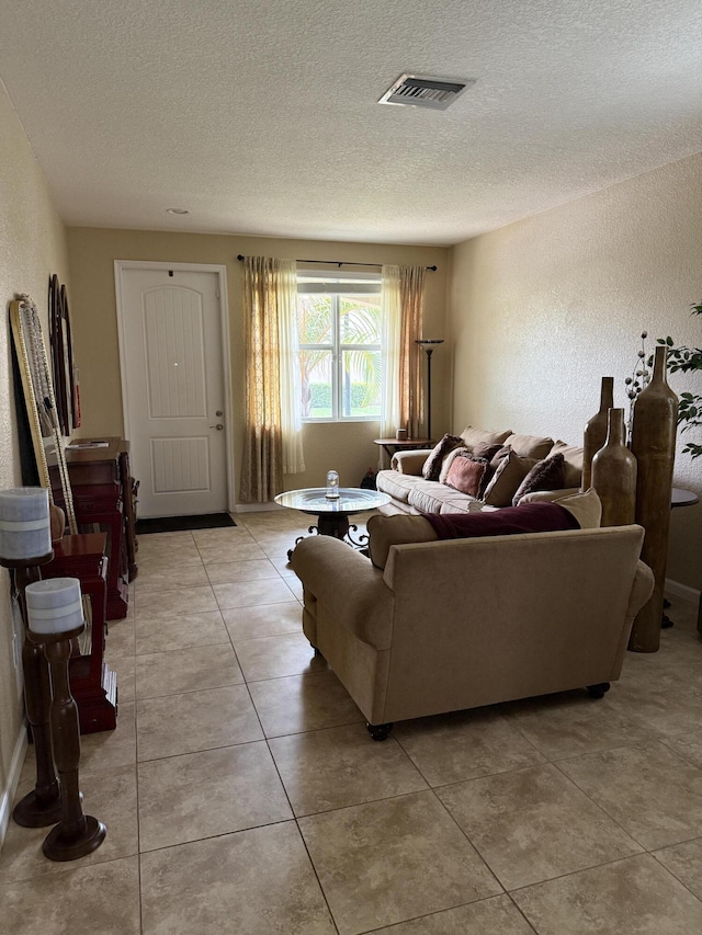 living area with light tile patterned floors, visible vents, a textured ceiling, and a textured wall