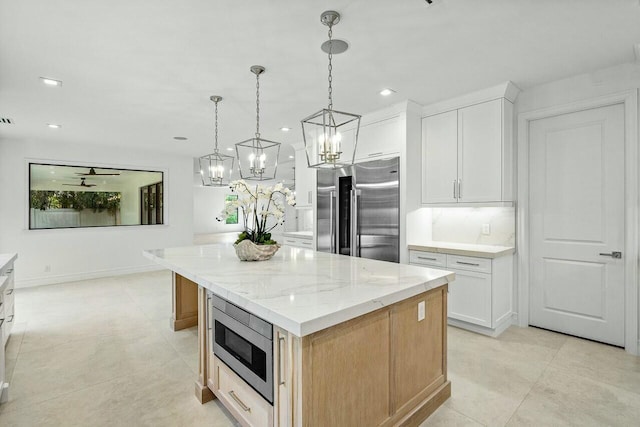 kitchen with light stone counters, built in appliances, white cabinets, and a center island