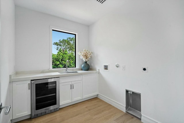 laundry room featuring beverage cooler, gas dryer hookup, light wood-type flooring, hookup for an electric dryer, and a sink