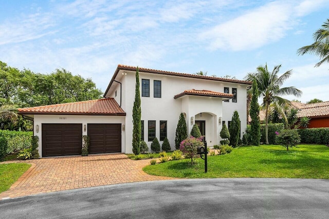 mediterranean / spanish-style house featuring a front yard, a tiled roof, an attached garage, and stucco siding