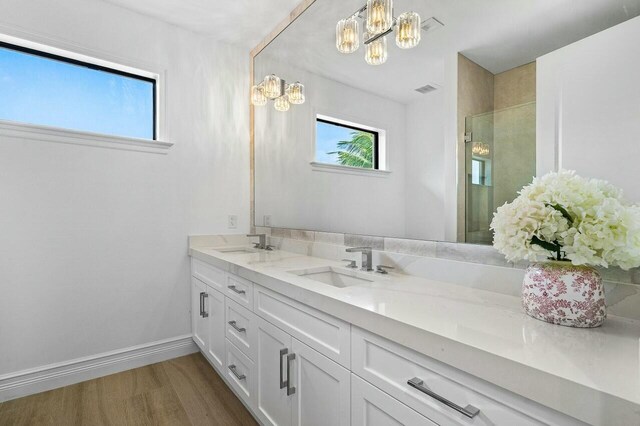 bathroom featuring a sink, a stall shower, wood finished floors, and double vanity