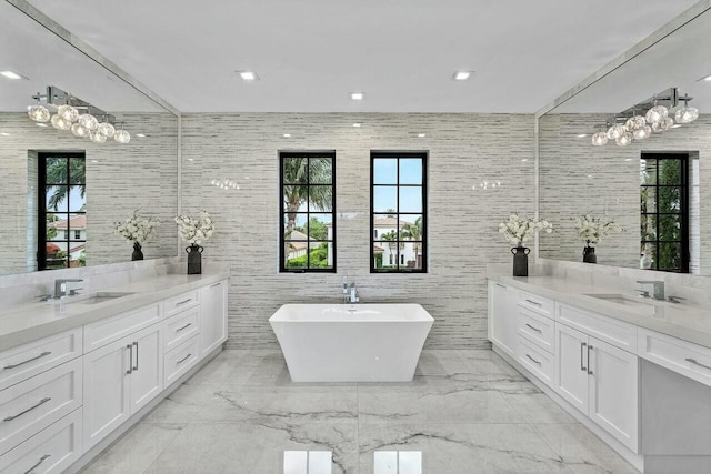 bathroom with a freestanding bath, two vanities, marble finish floor, and a sink