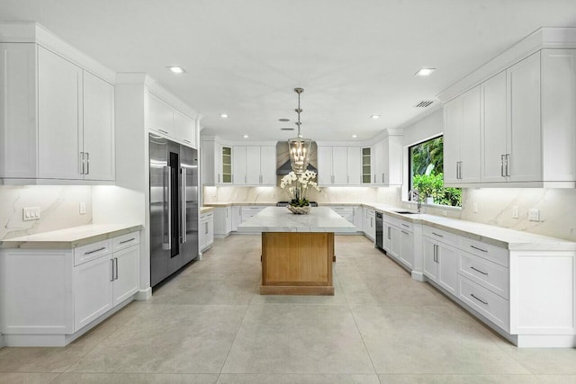 kitchen featuring wall chimney range hood, tasteful backsplash, built in fridge, and a center island