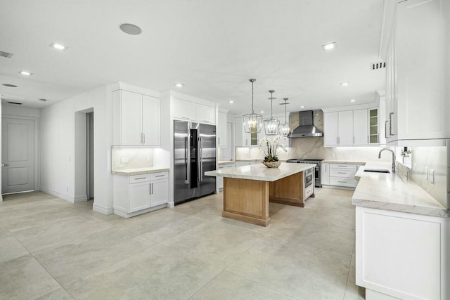 kitchen with backsplash, a kitchen island, wall chimney range hood, premium appliances, and a sink