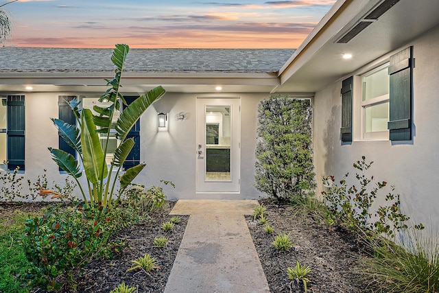 entrance to property with stucco siding and roof with shingles