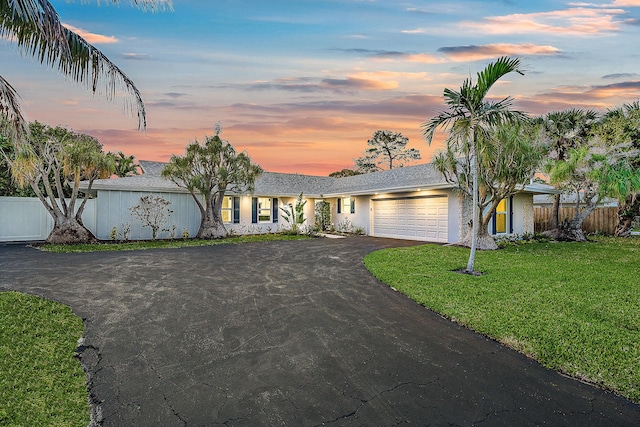 view of front facade with an attached garage, fence, aphalt driveway, and a lawn