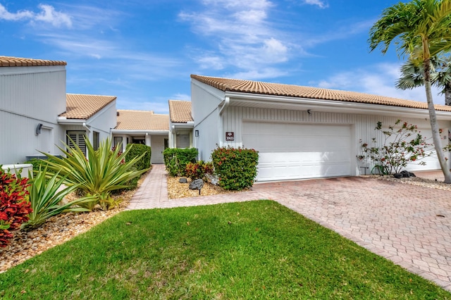 view of front facade featuring a garage, decorative driveway, a front yard, and a tile roof