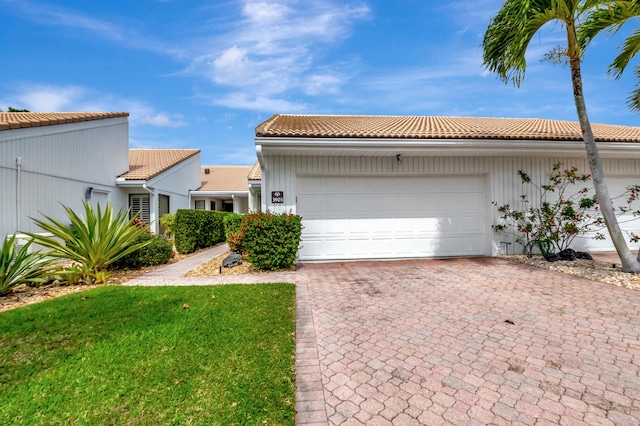 view of front of property featuring a garage, a front yard, decorative driveway, and a tiled roof