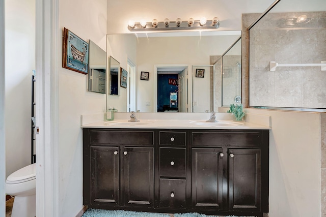 bathroom with double vanity, toilet, a tile shower, and a sink