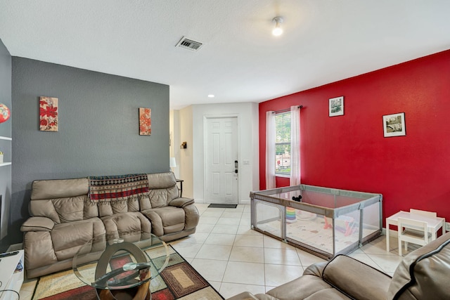 living room with an accent wall, light tile patterned flooring, visible vents, and baseboards