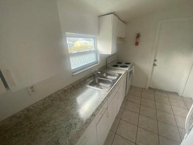 kitchen featuring white electric range oven, white cabinets, a sink, and light tile patterned flooring