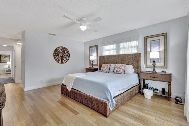 bedroom with light wood-type flooring, ceiling fan, baseboards, visible vents, and a textured ceiling